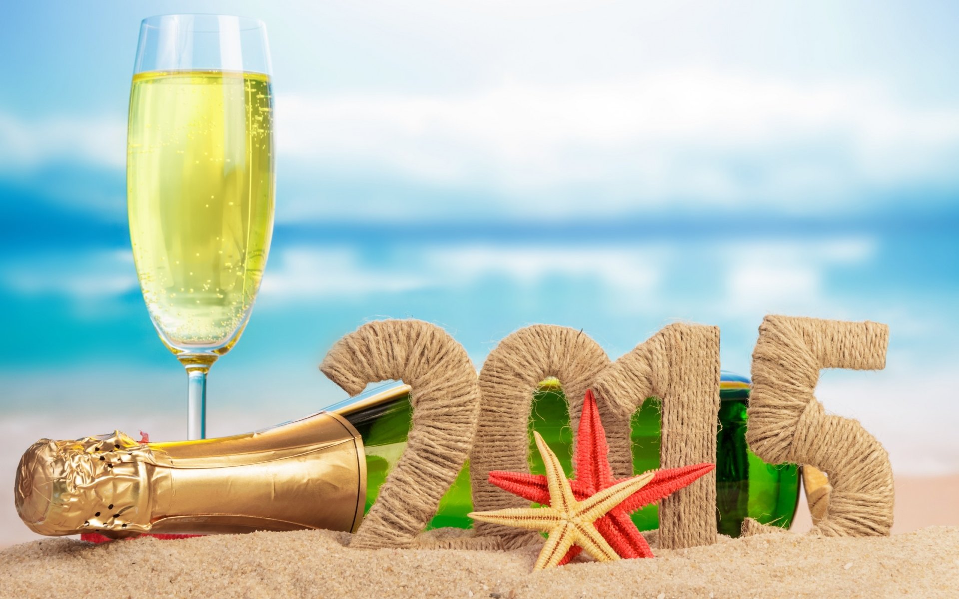 HD desktop wallpaper showing a New Year 2015 celebration with a champagne bottle, glass, and sandy beach setting, featuring party and holiday vibes.
