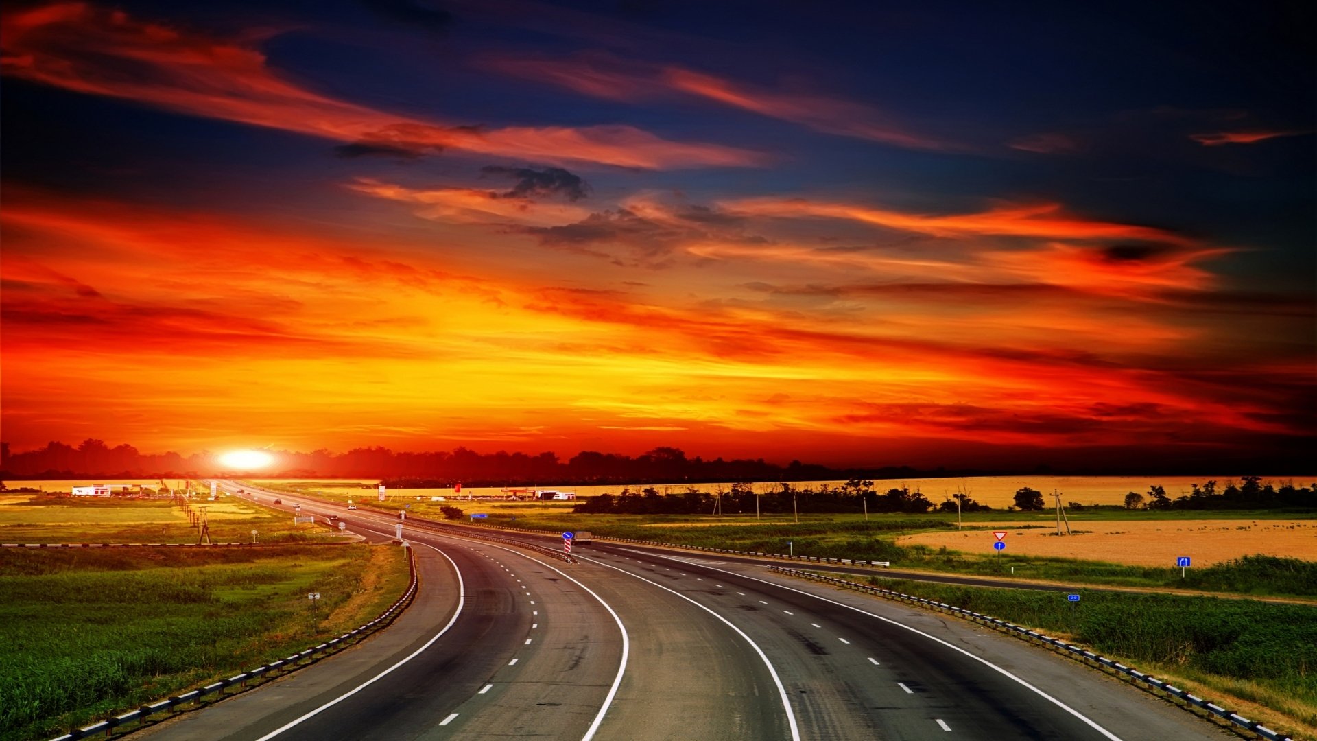 A vibrant sunset illuminates the sky over a winding road, creating a stunning man-made landscape. This HD image serves as an impressive desktop wallpaper and background.