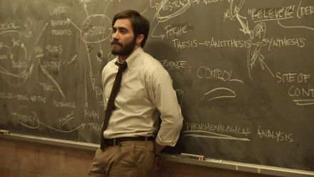 HD PC desktop wallpaper from the movie Enemy: a bearded man in a shirt and loosened tie leans against a chalkboard scrawled with diagrams and notes.
