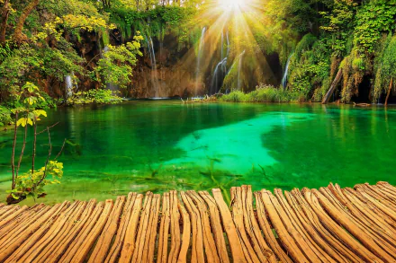 HD wallpaper of a vibrant scene at Plitvice Lakes National Park, Croatia featuring a waterfall, emerald lake, sun rays, and a wooden pathway.