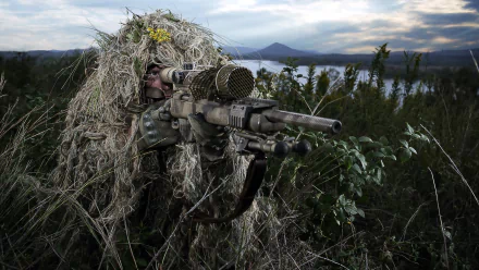 A camouflaged sniper with a rifle is positioned in a natural setting, capturing the essence of military precision. This HD image serves as an engaging desktop wallpaper.