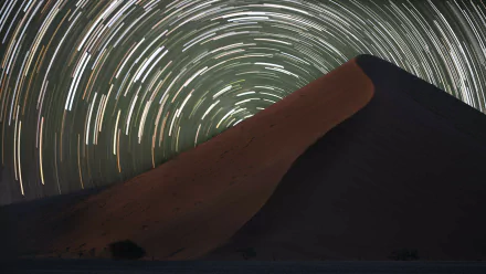 A stunning star trail time-lapse over a desert dune, showcasing a mesmerizing sci-fi landscape filled with swirling stars. Perfect HD wallpaper for lovers of the cosmos.