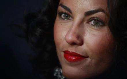 Close-up of Mexican actress Bárbara Mori, showcasing her striking features with dark, curly hair and bold red lips, set against a dark background. HD desktop wallpaper.