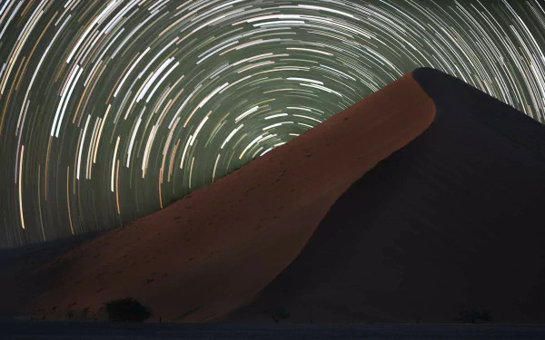 A stunning star trail time-lapse over a desert dune, showcasing a mesmerizing sci-fi landscape filled with swirling stars. Perfect HD wallpaper for lovers of the cosmos.