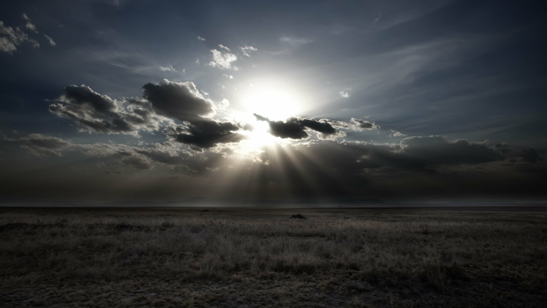 A dramatic nature scene with sunbeams breaking through dark clouds over a vast, open landscape, captured in stunning 4K Ultra HD quality for PC desktop wallpaper.