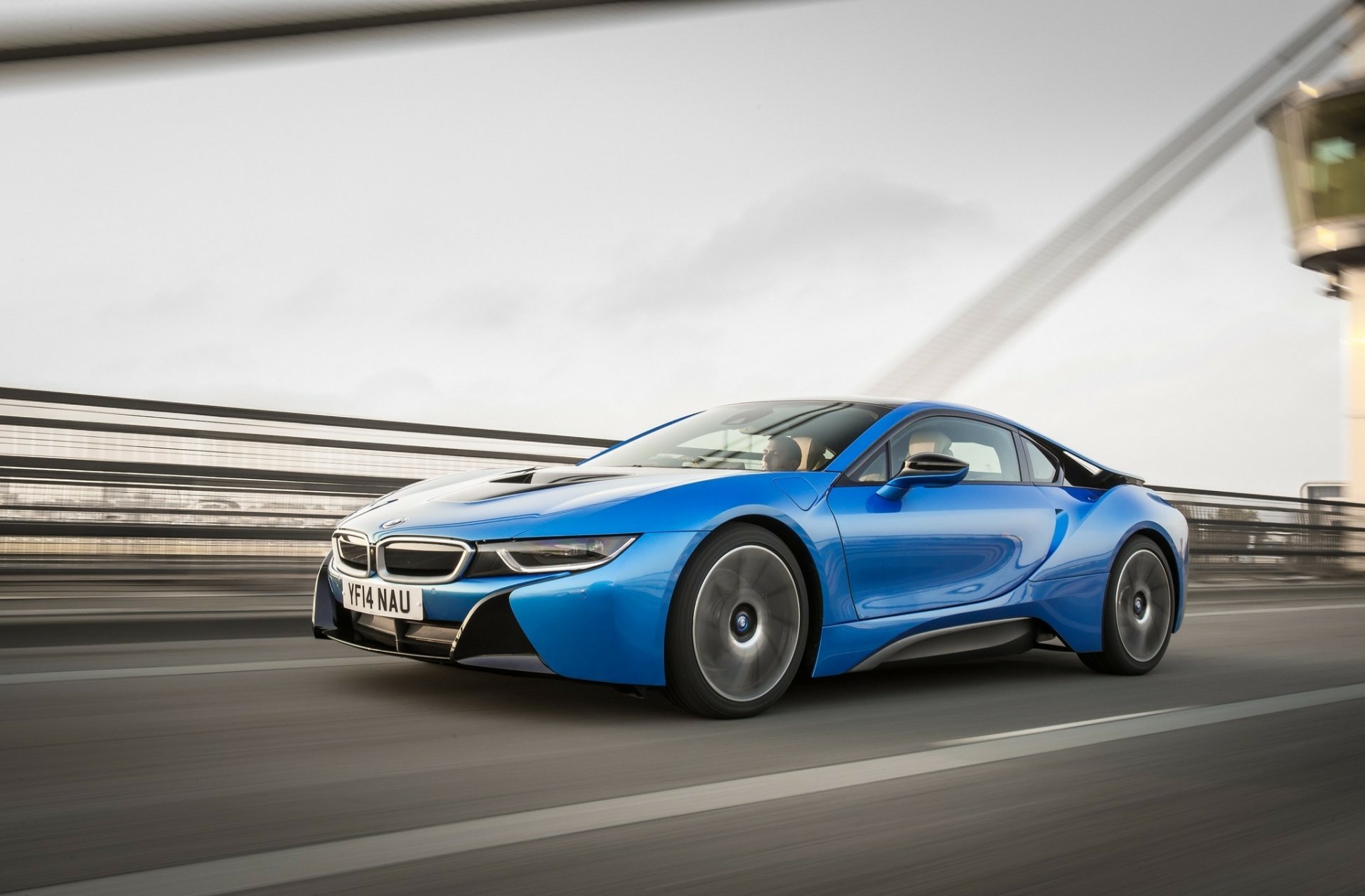 HD PC desktop wallpaper featuring a blue BMW i8 vehicle speeding on a road with a blurred bridge background.