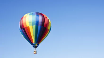A vibrant hot air balloon with multicolored stripes floats against a clear blue sky, offering a stunning HD desktop wallpaper and background.