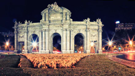 HD desktop wallpaper featuring the illuminated Puerta de Alcalá monument at night, showcasing its detailed man-made architecture and surrounding city lights.