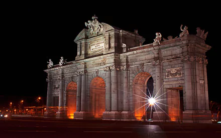 HD desktop wallpaper showcasing the Puerta de Alcalá monument illuminated at night, highlighting its intricate man-made architectural details against a dark sky.