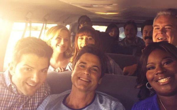 HD wallpaper featuring the Parks and Recreation cast with characters Chris Traeger and Leslie Knope smiling inside a vehicle.