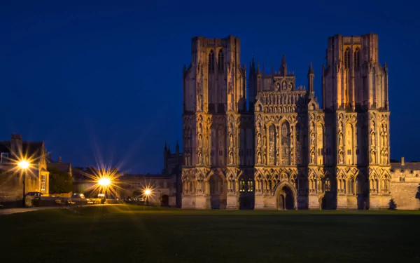 HD desktop wallpaper featuring Wells Cathedral illuminated against a deep blue night sky, showcasing its intricate religious architecture and historic grandeur.