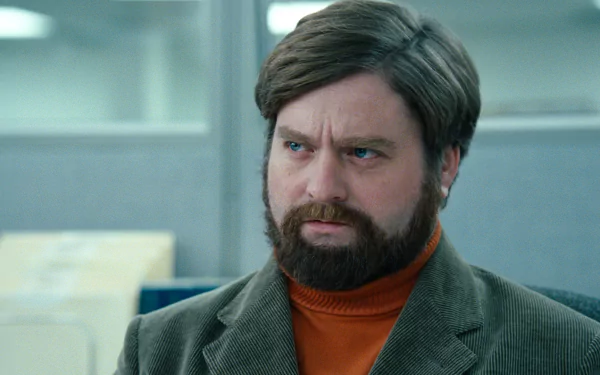 HD desktop wallpaper featuring a bearded man with a contemplative expression, wearing a jacket over an orange turtleneck.