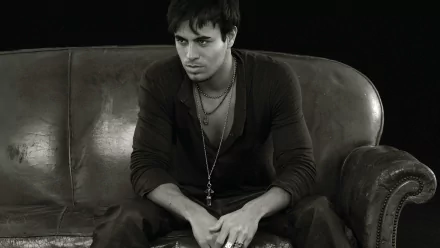 Black and white HD wallpaper of Enrique Iglesias sitting on a leather couch, exuding a contemplative expression. Tags: music, Enrique Iglesias.
