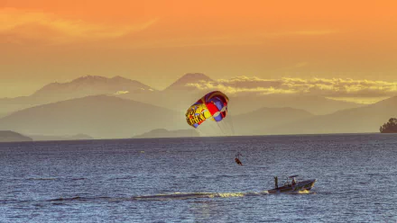 4K Ultra HD desktop wallpaper showing a vibrant parasailing scene over calm ocean waters with mountains and a colorful sunset sky in the background.