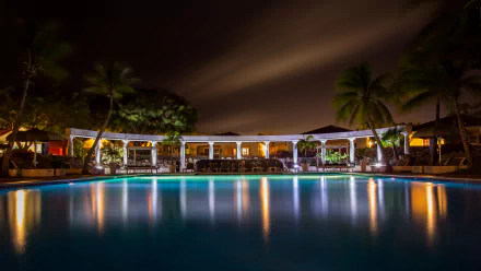 4K Ultra HD wallpaper of a luxurious villa at night with a large illuminated man-made pool in the foreground under a dark, cloudy sky.