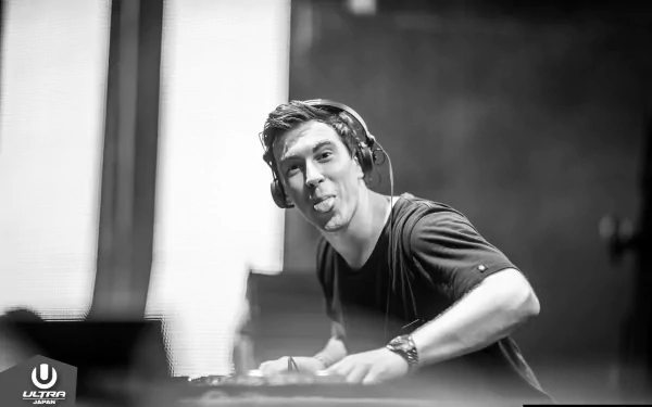 Black-and-white HD PC desktop wallpaper of an electronic music DJ at a booth, headphones on, playfully sticking out his tongue.