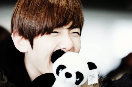 A cheerful person with short brown hair smiles widely while playfully holding a panda plush toy, set against a soft background. This image serves as a vibrant EXO-themed HD wallpaper.
