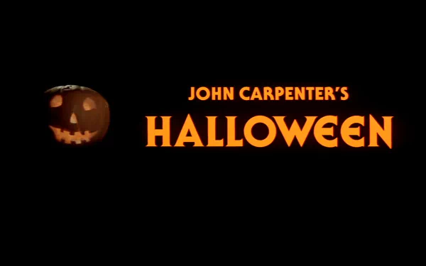 A dark background featuring the iconic title of John Carpenter's Halloween (1978) in bold orange, with a carved pumpkin on the side, creating a spooky atmosphere for a desktop wallpaper.