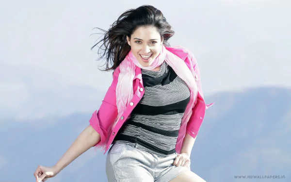 Tamannaah Bhatia poses stylishly in a vibrant pink jacket against a scenic backdrop, capturing the essence of Bollywood glamour in this HD desktop wallpaper.