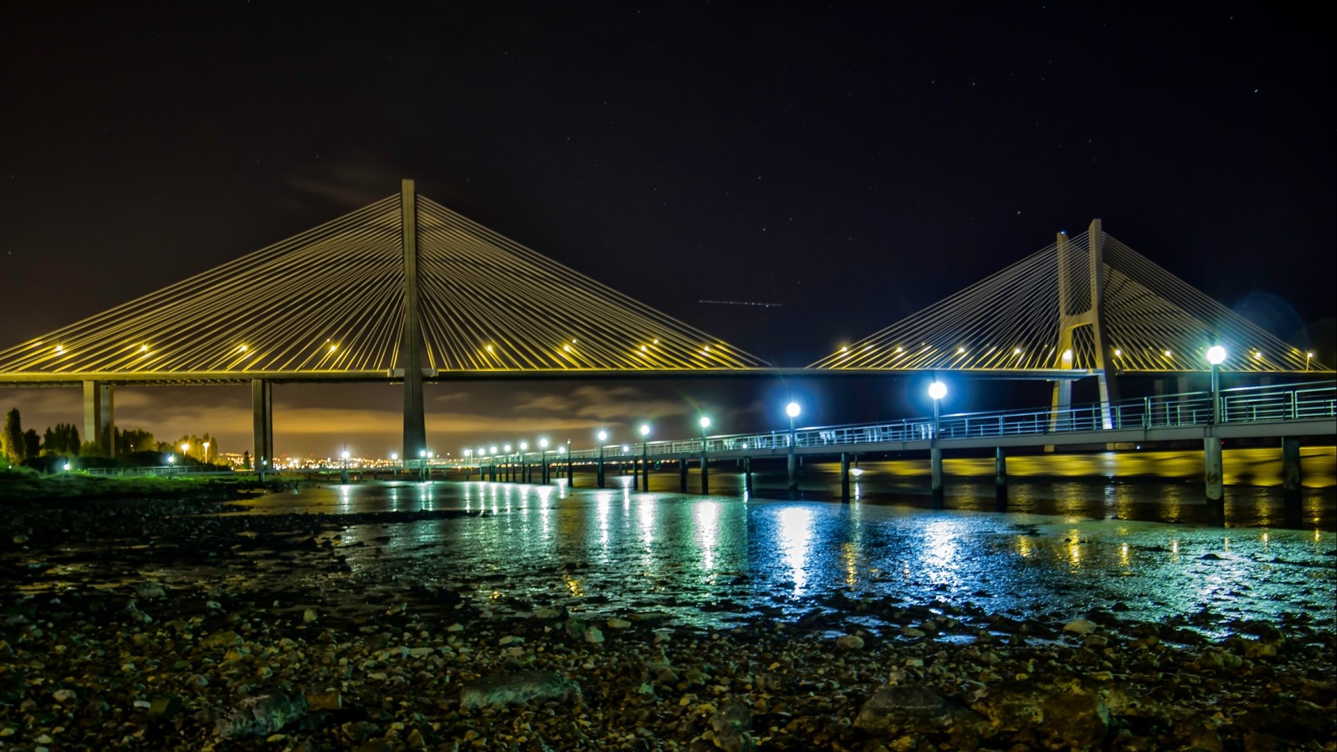 Night view of the illuminated Vasco da Gama Bridge over calm water, captured as a high-definition man-made structure for a PC desktop wallpaper background.