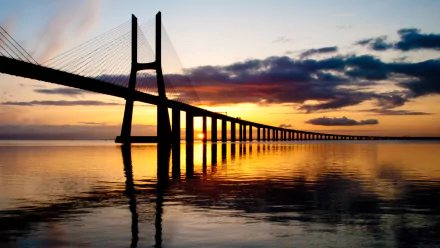 Vasco da Gama Bridge cable-stayed span at sunrise, golden reflections on calm water; man-made structure framed as a 2K Quad HD PC desktop wallpaper background.