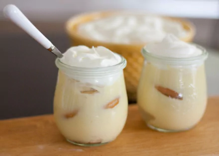 HD desktop wallpaper featuring two glass jars of creamy banana pudding topped with whipped cream on a wooden surface, showcasing a delicious dessert.