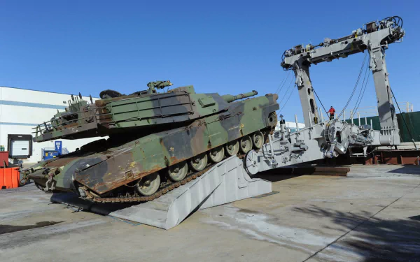 An M1A1 Abrams tank rests on a ramp, showcasing its military design against a clear blue sky, set in an industrial environment as a striking HD desktop wallpaper.
