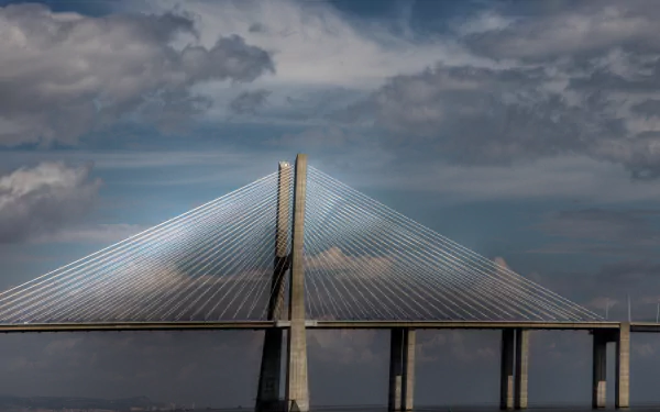 Man-made Vasco da Gama Bridge spanning calm water beneath dramatic clouds — 2K Quad HD PC desktop wallpaper/background.
