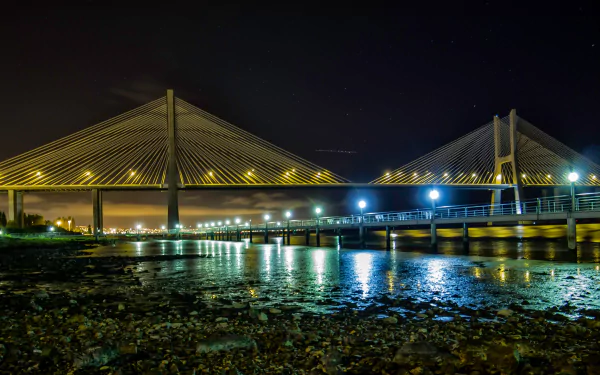 Night view of the illuminated Vasco da Gama Bridge over calm water, captured as a high-definition man-made structure for a PC desktop wallpaper background.