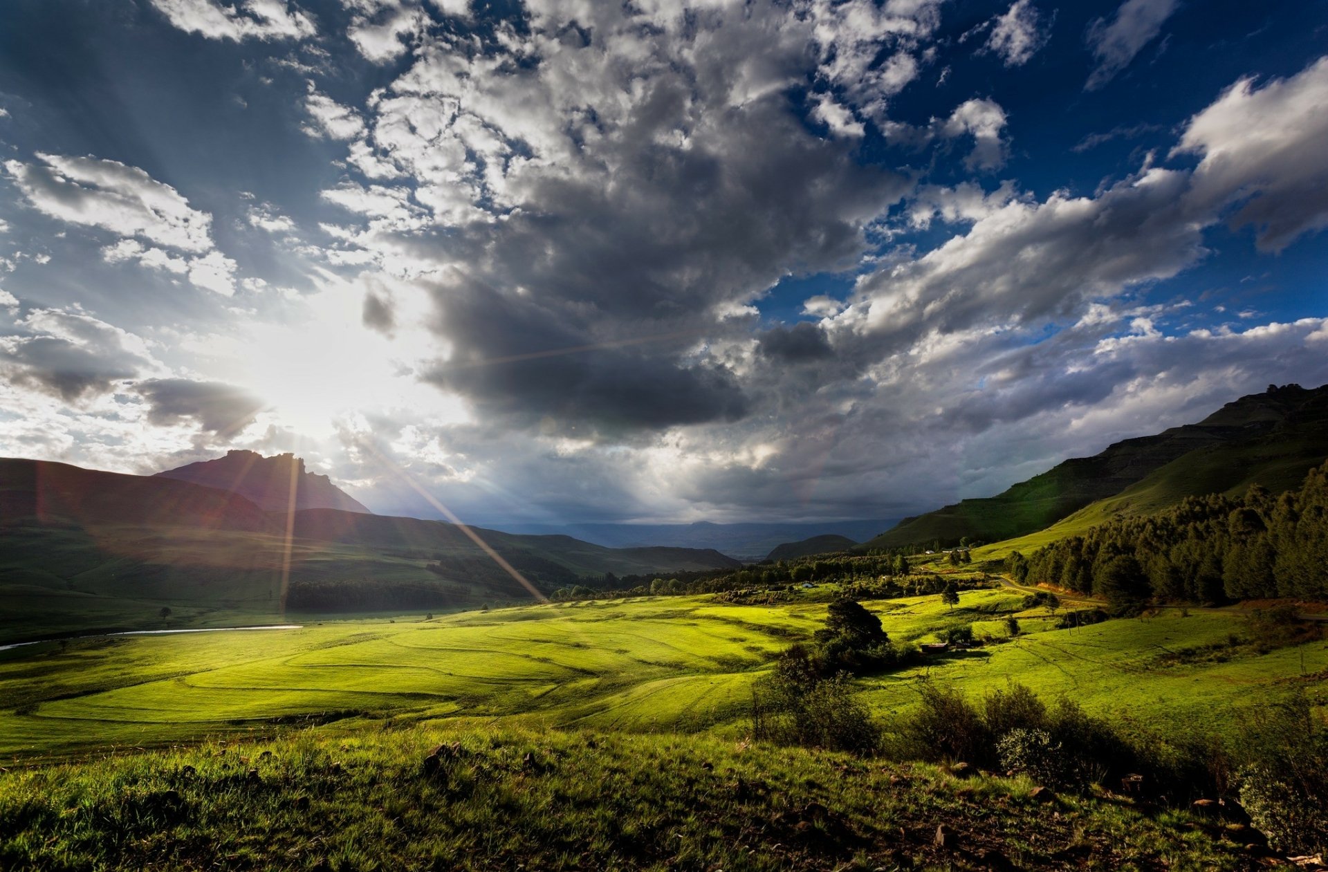 Sunlight breaks through dramatic clouds over a lush green landscape in South Africa, creating a vibrant natural scene captured in HD for a desktop wallpaper background.