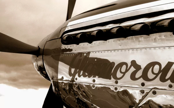 HD desktop wallpaper: close-up of a polished military propeller aircraft nose with reflective chrome skin and vintage aircraft nose art script, set against a cloudy sky background.
