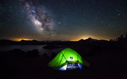 A vibrant green tent glows under the stunning Milky Way, set against a serene lakeside backdrop, showcasing the beauty of camping and astrophotography in high definition.
