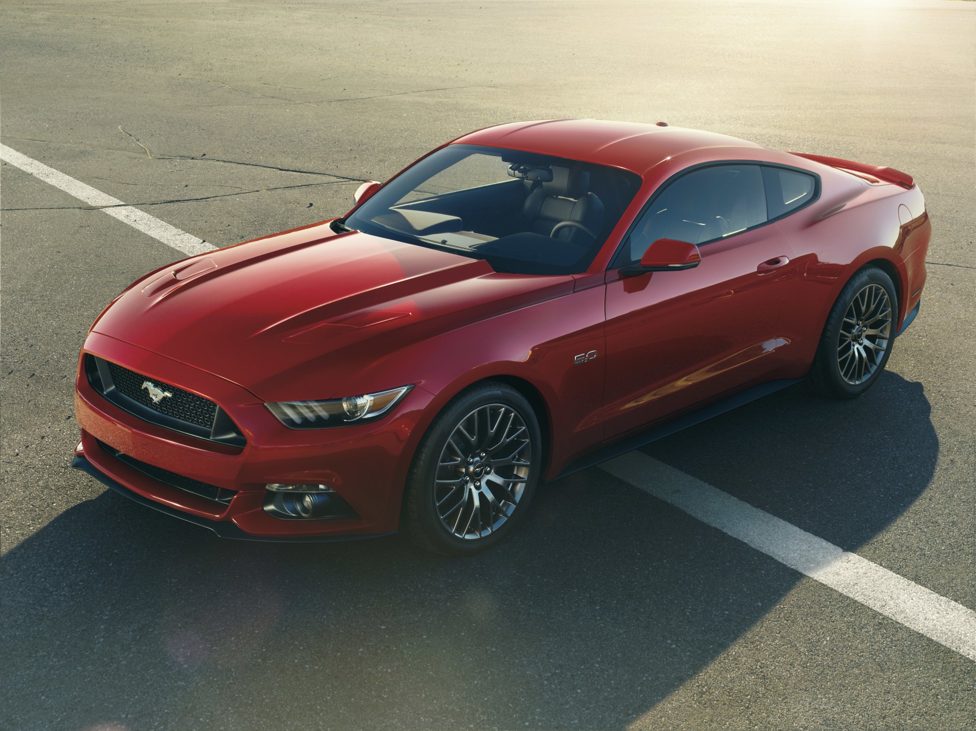 A sleek red 2015 Ford Mustang, showcasing its sporty design, parked on a sunlit asphalt surface, serves as a striking HD desktop wallpaper and background.