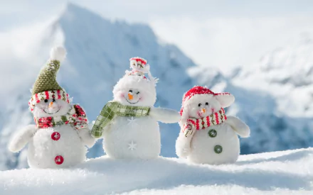 Three cheerful snowmen wearing colorful scarves and hats stand in a snowy landscape, with majestic mountains in the background. A delightful HD photography wallpaper.