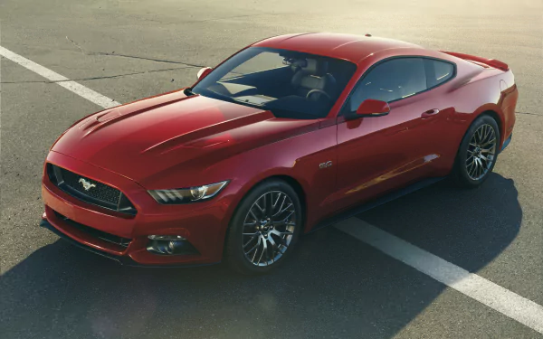 A sleek red 2015 Ford Mustang, showcasing its sporty design, parked on a sunlit asphalt surface, serves as a striking HD desktop wallpaper and background.