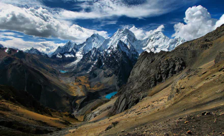 Majestic snow-capped Andes Mountains rise under a dramatic sky, with clouds swirling over rugged peaks and vibrant valleys. A stunning natural landscape from Peru.