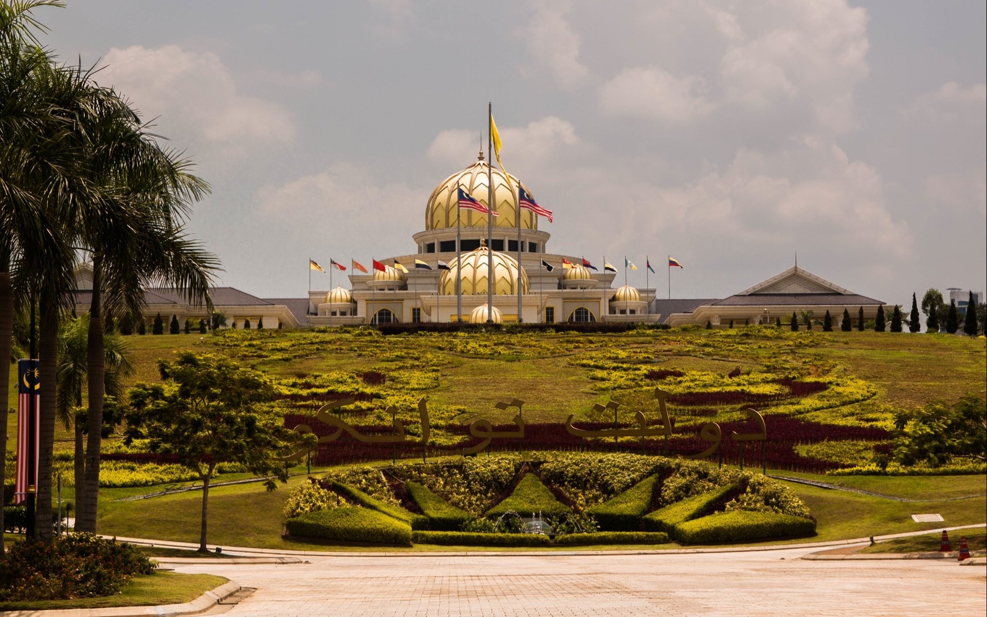 HD desktop wallpaper of the man-made Istana Negara in Jakarta — a grand domed state palace atop terraced lawns and sculpted hedges under a cloudy sky.