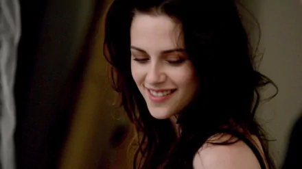 HD wallpaper of actress Kristen Stewart with a smile on her face. Her hair is tousled, and she is wearing a black top, with a soft background adding to the serene ambiance.