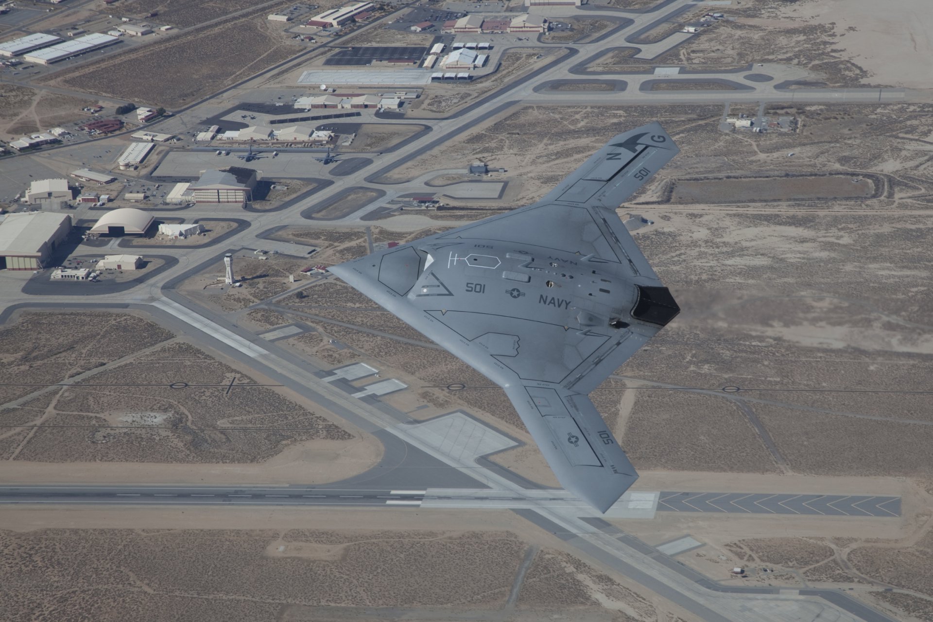 Aerial view of the Northrop Grumman X-47B military drone flying over an airbase, captured in HD for a desktop wallpaper and background.