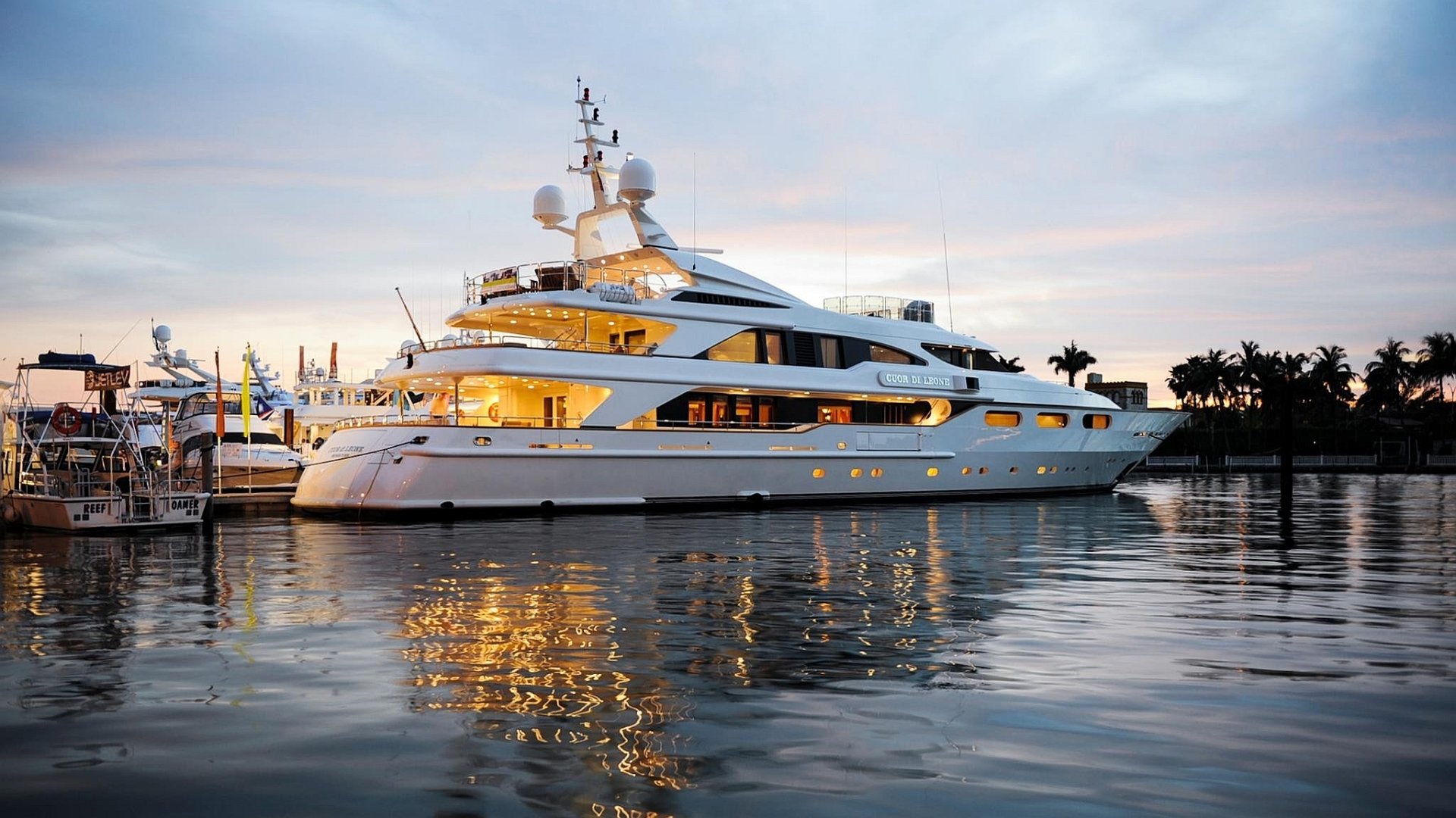 HD desktop wallpaper featuring a luxurious yacht moored at a marina during sunset, with calm waters reflecting the vehicle's lights and surroundings.