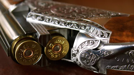 Close-up HD desktop wallpaper of a man-made shotgun showcasing intricate silver engravings and two shotgun shells loaded in the barrel.