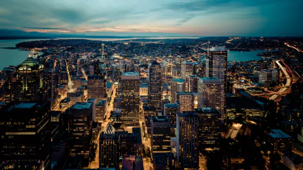A vibrant HD desktop wallpaper showcasing the man-made skyline of Seattle at dusk, with illuminated buildings and a calm waterfront under a colorful sky.