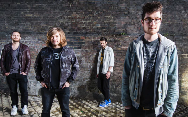 HD desktop wallpaper featuring the English rock band Bastille standing against a brick wall, showcasing their casual music style and band members.