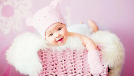 A cute baby smiling in a pink bear hat, nestled in a soft, fluffy setting. This heartwarming image makes a charming 4K Ultra HD desktop wallpaper or background.