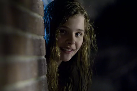 A still from the movie *Let Me In*, featuring a girl with wet, tousled hair peeking around a brick wall, creating a haunting and eerie atmosphere. HD PC desktop wallpaper and background.