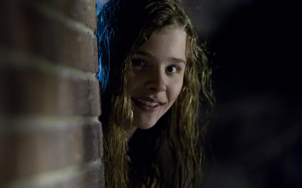 A still from the movie *Let Me In*, featuring a girl with wet, tousled hair peeking around a brick wall, creating a haunting and eerie atmosphere. HD PC desktop wallpaper and background.