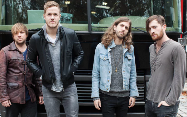 Four members of the American alternative band Imagine Dragons stand in front of a tour bus, showcasing their unique style in this vibrant 4K Ultra HD desktop wallpaper.