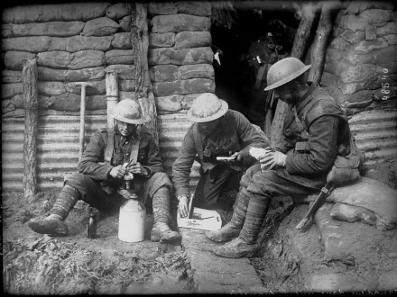 Three soldiers in World War I, seated in a trench, engage with their equipment. The image captures a moment of camaraderie amid the realities of military life. HD wallpaper background.