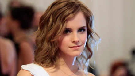 HD desktop wallpaper and background featuring celebrity Emma Watson with a soft smile and wavy hair, set against a blurred, indoor backdrop.