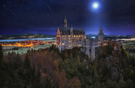 A stunning night scene of Neuschwanstein Castle in Germany, illuminated under a starry sky, with a bright moon and a meteor streaking across the horizon. A captivating desktop wallpaper.